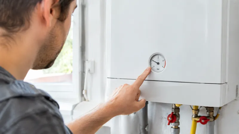 Hand zeigt auf das runde Manometer einer modernen weißen Gastherme an der Wand eines sauberen Hauswirtschaftsraums