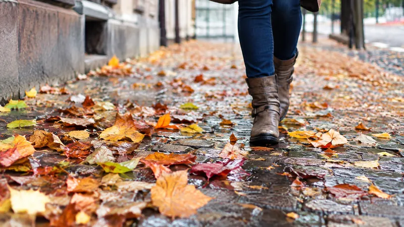 Nasses Herbstlaub auf Kopfsteinpflaster, ein Fußgänger in Stiefeln setzt vorsichtig einen Schritt vor den anderen