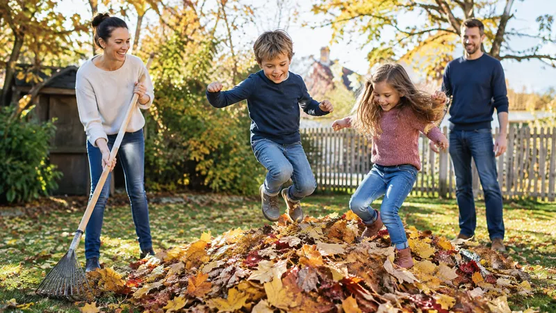 Familie recht gemeinsam buntes Herbstlaub zusammen, zwei Kinder springen lachend in einen großen Laubhaufen