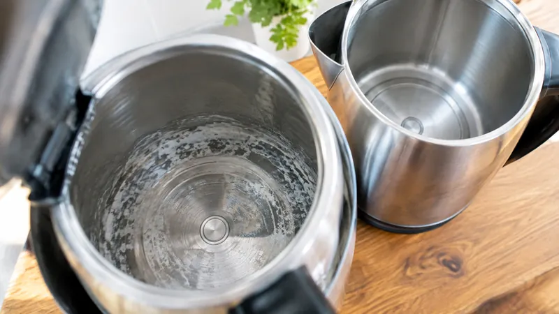 Zwei Edelstahl-Wasserkocher nebeneinander, im vorderen weiße Kalkablagerungen am Boden, der hintere innen blank